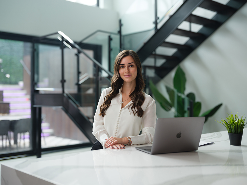 Courtier-Immobilier-Otterburn-Park-Carolyne-Larocque-Open-Laptop-Plant-Marble-Table-From-Left